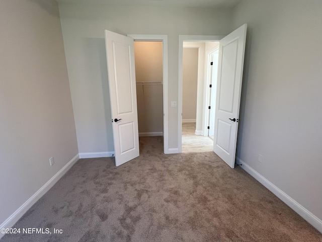 unfurnished bedroom with a walk in closet, light carpet, and a closet