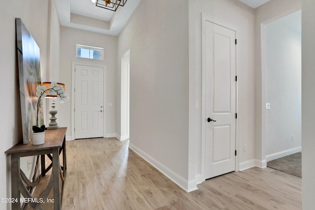 foyer entrance with light wood finished floors, a raised ceiling, and baseboards