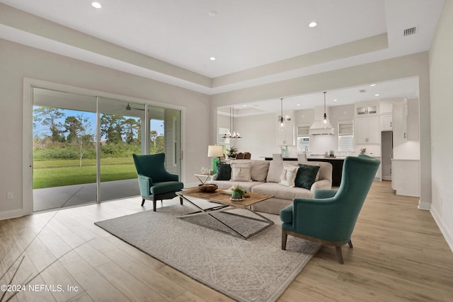 living room with an inviting chandelier, light wood-type flooring, and a tray ceiling