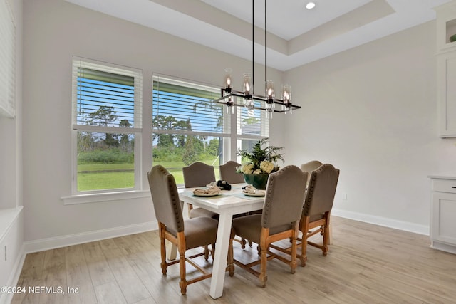 dining area with light hardwood / wood-style floors, a raised ceiling, and a chandelier