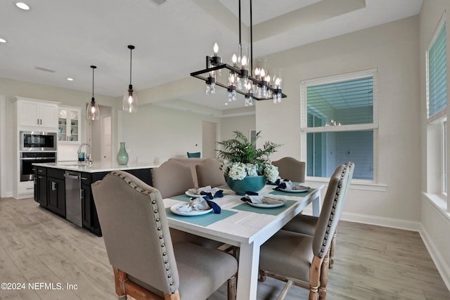 dining room featuring a raised ceiling, sink, and light wood-type flooring