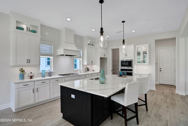 kitchen with white cabinets, an island with sink, and custom exhaust hood