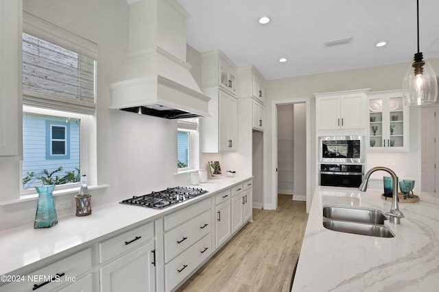 kitchen with glass insert cabinets, premium range hood, a sink, and hanging light fixtures