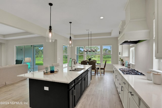 kitchen featuring custom exhaust hood, stainless steel gas cooktop, a kitchen island with sink, pendant lighting, and white cabinetry