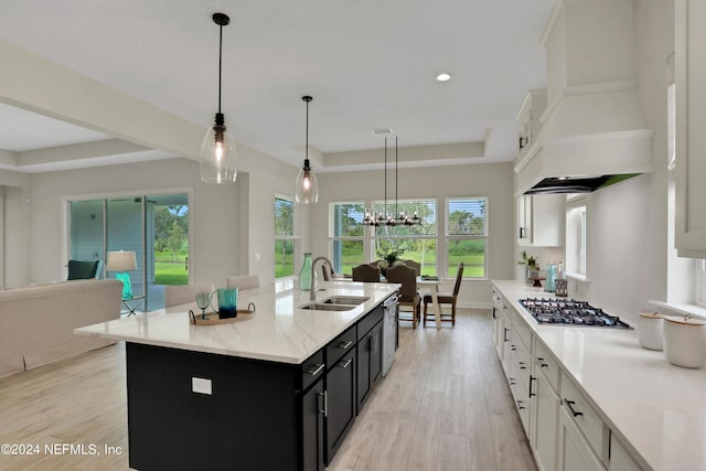 kitchen with a center island with sink, a raised ceiling, custom range hood, white cabinets, and dark cabinets