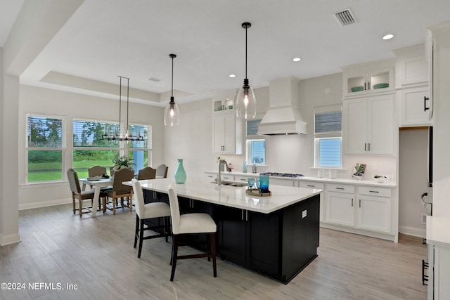 kitchen featuring a center island with sink, white cabinets, pendant lighting, and custom range hood