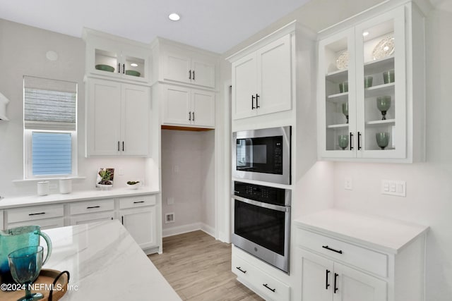 kitchen featuring oven, white cabinets, light wood-type flooring, built in microwave, and glass insert cabinets