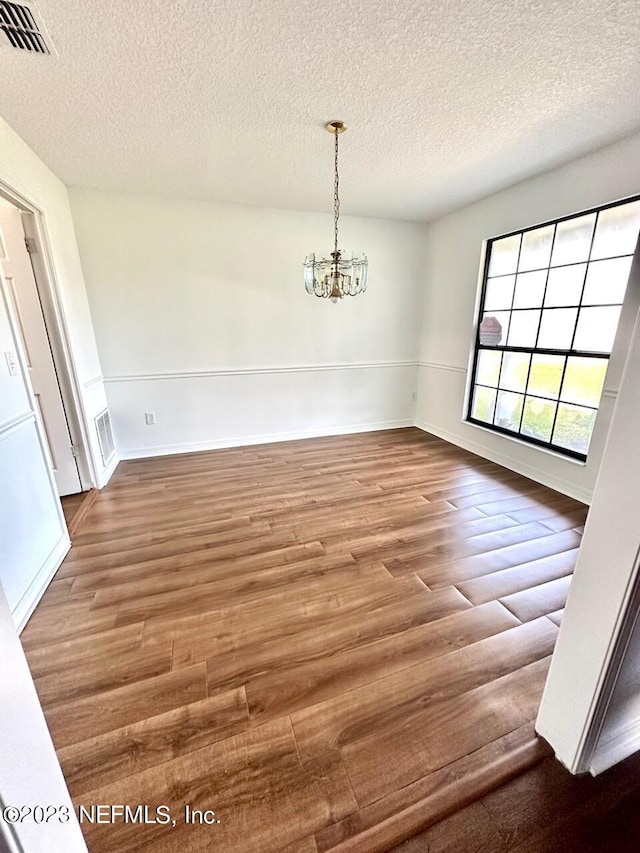 unfurnished dining area featuring hardwood / wood-style floors, a textured ceiling, and a chandelier