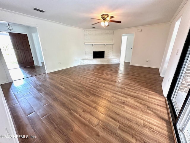 unfurnished living room featuring crown molding, ceiling fan, wood-type flooring, and a brick fireplace