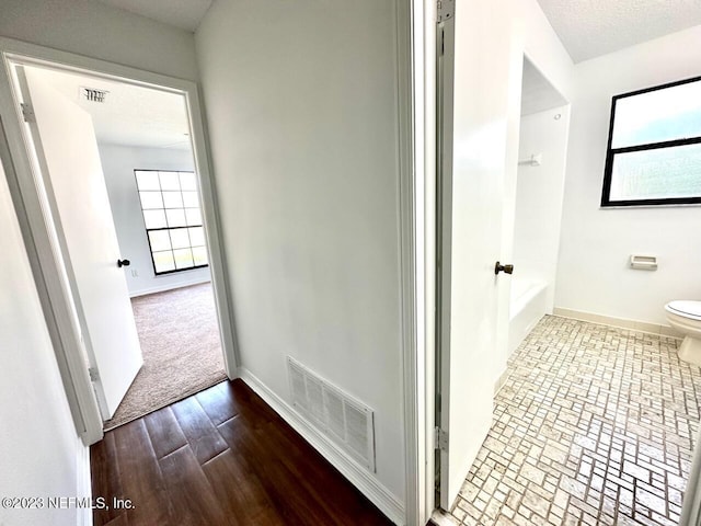 bathroom with a bathtub, a textured ceiling, hardwood / wood-style floors, and toilet