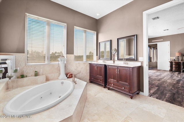 bathroom with a textured ceiling, plenty of natural light, vanity, and tiled bath