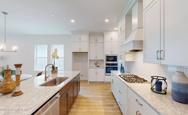 kitchen featuring stainless steel appliances, light wood-style flooring, white cabinets, a sink, and wall chimney exhaust hood