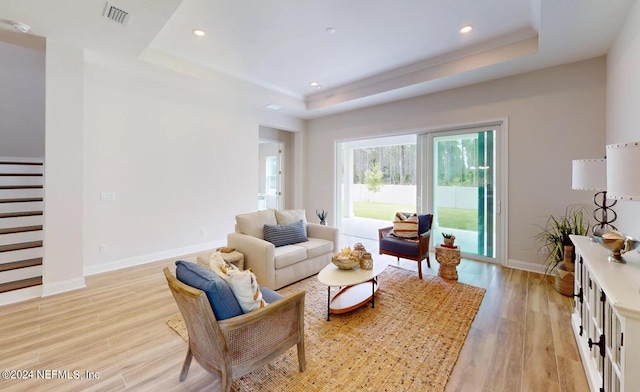 living room with light wood-style floors, a raised ceiling, visible vents, and baseboards