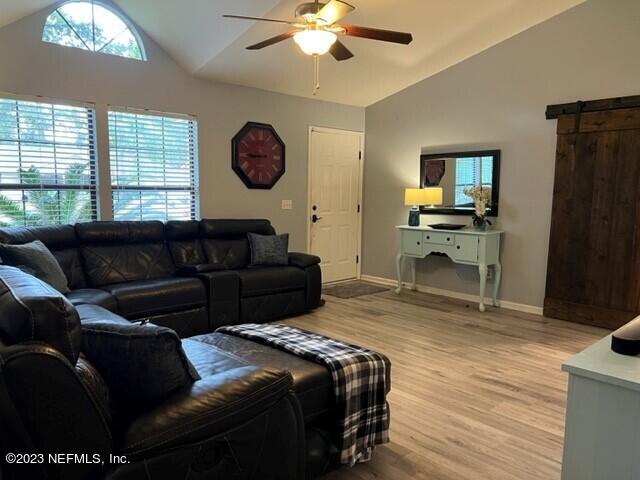 living room with vaulted ceiling, a barn door, ceiling fan, and light hardwood / wood-style flooring