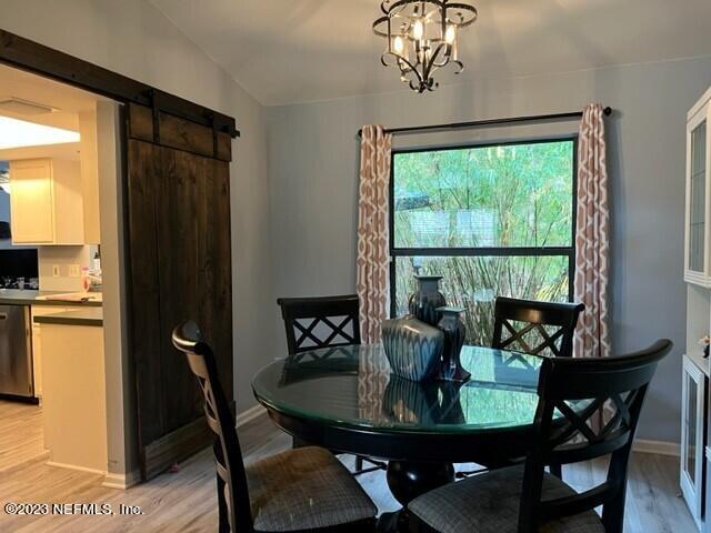 dining room with a barn door, a notable chandelier, and light hardwood / wood-style floors