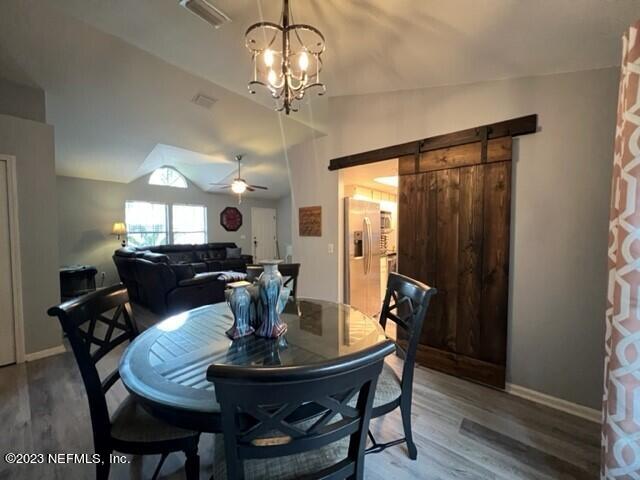 dining space featuring ceiling fan with notable chandelier, a barn door, vaulted ceiling, and hardwood / wood-style floors