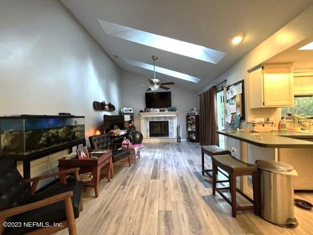 kitchen with lofted ceiling with skylight, a breakfast bar, white cabinets, ceiling fan, and light wood-type flooring