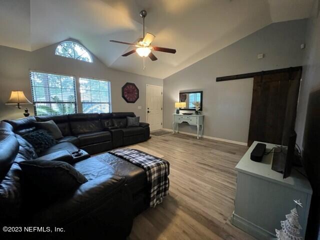 living room with high vaulted ceiling, a barn door, hardwood / wood-style floors, and ceiling fan