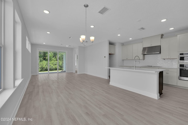 kitchen featuring an inviting chandelier, decorative light fixtures, decorative backsplash, a center island with sink, and light wood-type flooring