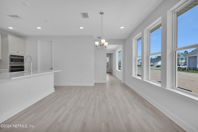 unfurnished living room with a textured ceiling, light hardwood / wood-style floors, an inviting chandelier, and sink