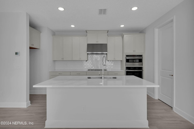 kitchen with ventilation hood, decorative backsplash, a center island with sink, white cabinets, and appliances with stainless steel finishes