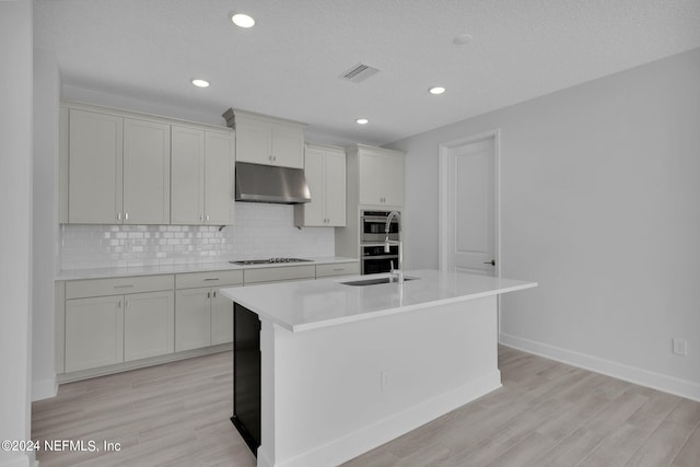 kitchen with a kitchen island with sink, white cabinets, sink, light hardwood / wood-style flooring, and stainless steel double oven