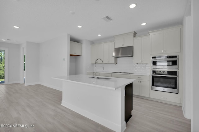 kitchen featuring white cabinetry, sink, a kitchen island with sink, black electric stovetop, and double wall oven