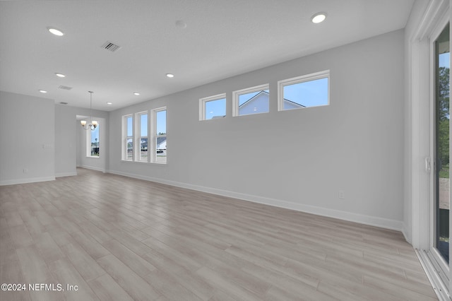 unfurnished room with light wood-type flooring, an inviting chandelier, and a healthy amount of sunlight