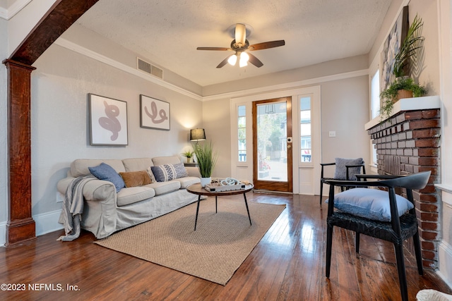 living room featuring a textured ceiling, dark wood-type flooring, visible vents, a ceiling fan, and a brick fireplace