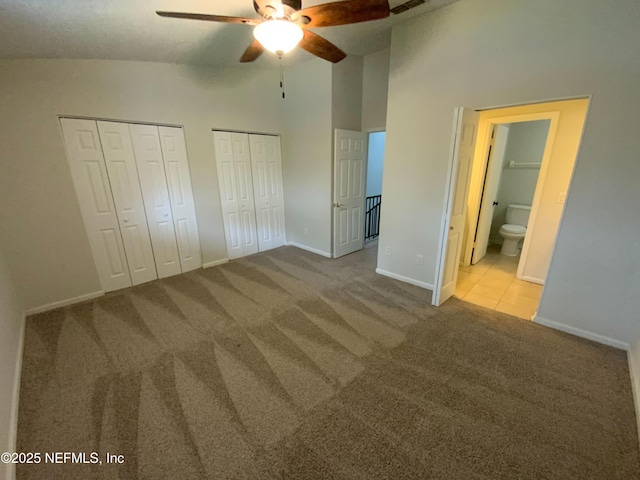 unfurnished bedroom with high vaulted ceiling, carpet flooring, visible vents, baseboards, and two closets