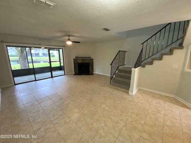 unfurnished living room featuring a ceiling fan, stairs, visible vents, and a tiled fireplace