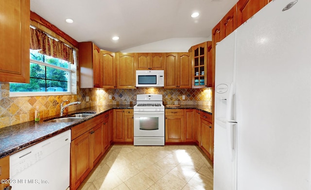 kitchen with decorative backsplash, white appliances, vaulted ceiling, sink, and dark stone countertops