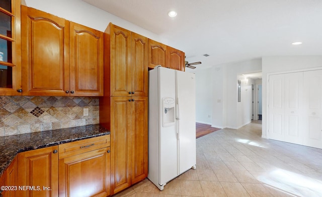 kitchen with ceiling fan, white refrigerator with ice dispenser, backsplash, and dark stone counters