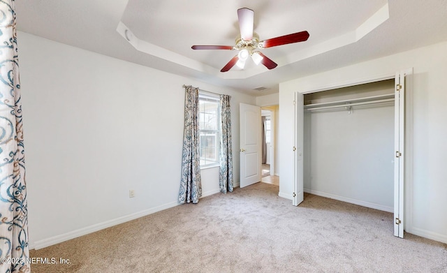 unfurnished bedroom featuring a closet, a raised ceiling, ceiling fan, and light colored carpet