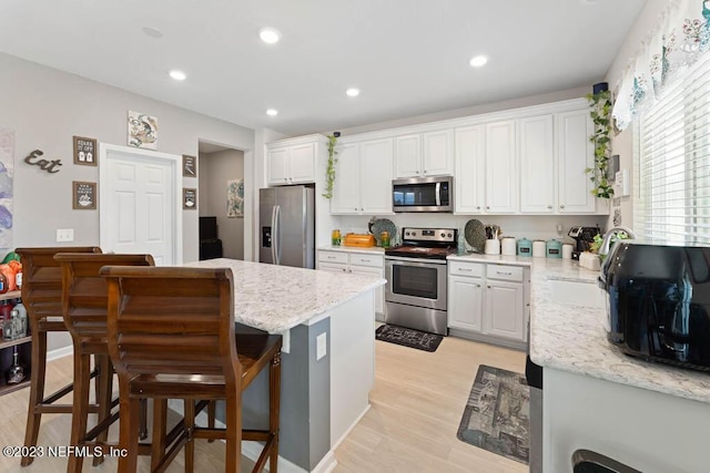 kitchen with a breakfast bar area, appliances with stainless steel finishes, white cabinetry, light stone counters, and light hardwood / wood-style floors