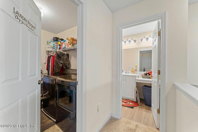 laundry area featuring washing machine and clothes dryer, light colored carpet, and a textured ceiling