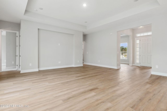 unfurnished living room with a raised ceiling and light hardwood / wood-style flooring