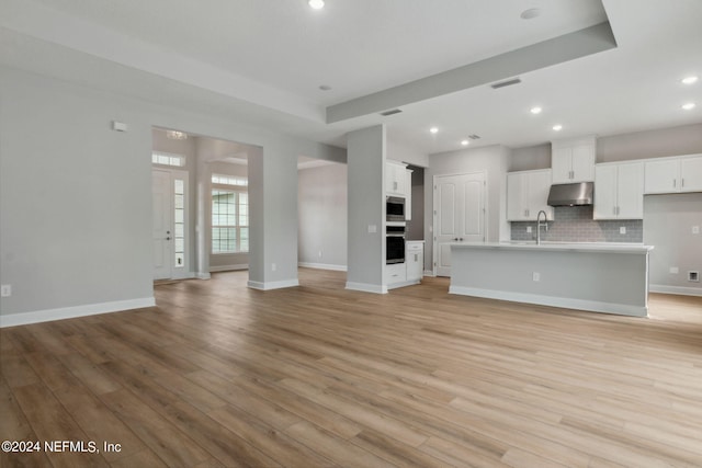 unfurnished living room with light wood-type flooring, a tray ceiling, and sink