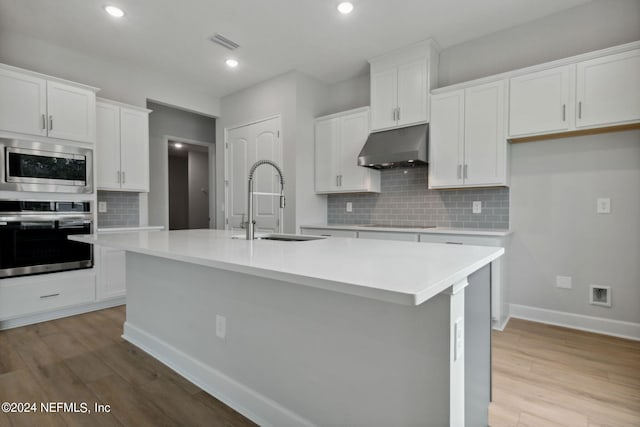 kitchen with sink, stainless steel appliances, an island with sink, white cabinets, and light wood-type flooring