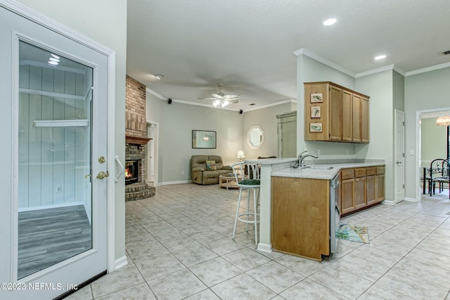 kitchen featuring a breakfast bar area, brown cabinets, open floor plan, a brick fireplace, and a sink