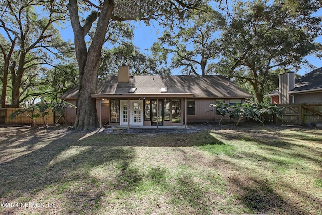 back of house featuring french doors, a yard, a chimney, a sunroom, and a fenced backyard