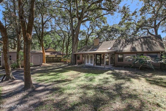 rear view of property with an outbuilding, french doors, a chimney, a storage unit, and fence