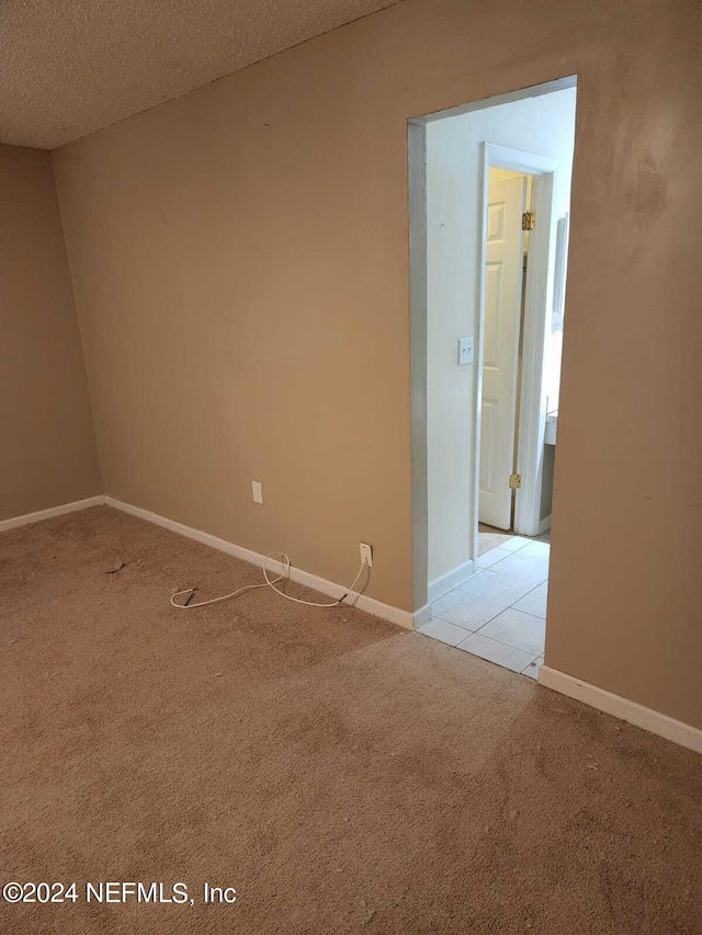 empty room featuring baseboards, a textured ceiling, and light colored carpet