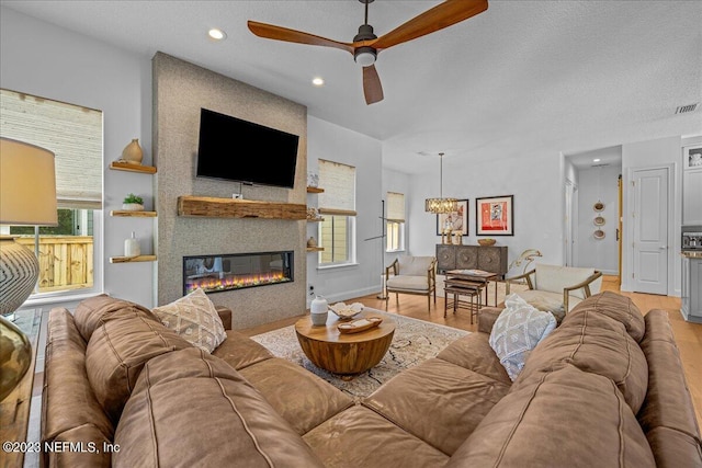 living room with ceiling fan, a large fireplace, a textured ceiling, and light hardwood / wood-style flooring