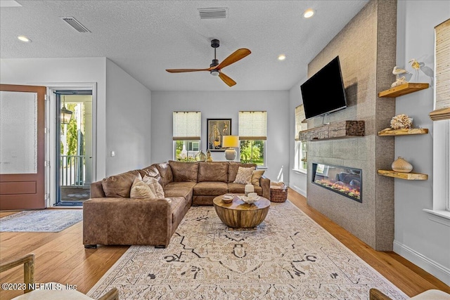 living room featuring a tile fireplace, light hardwood / wood-style floors, a textured ceiling, and a wealth of natural light