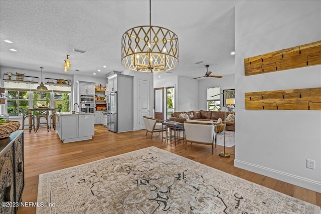 living room with sink, ceiling fan with notable chandelier, a textured ceiling, and light wood-type flooring