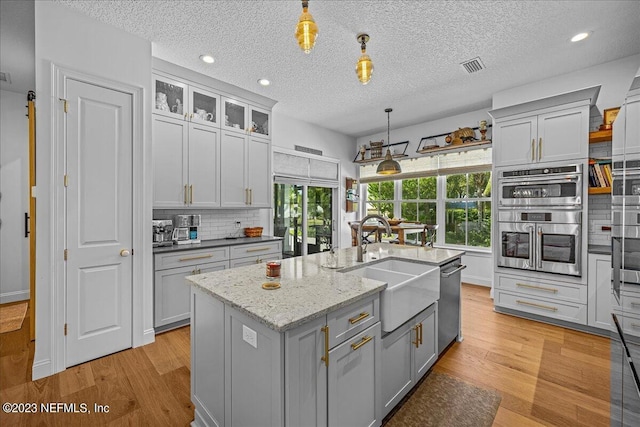 kitchen with appliances with stainless steel finishes, sink, light wood-type flooring, and decorative light fixtures