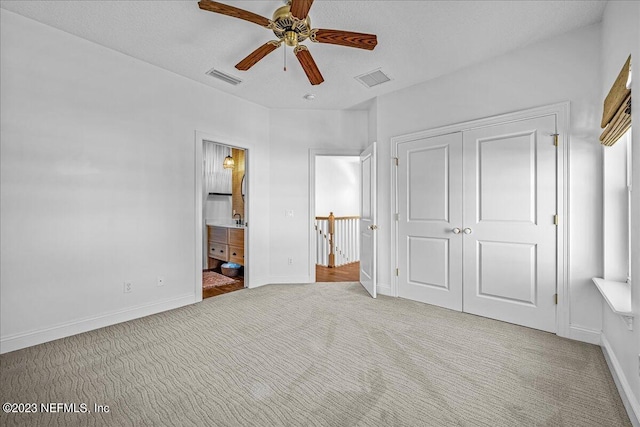 unfurnished bedroom featuring light colored carpet, a closet, ceiling fan, and ensuite bathroom