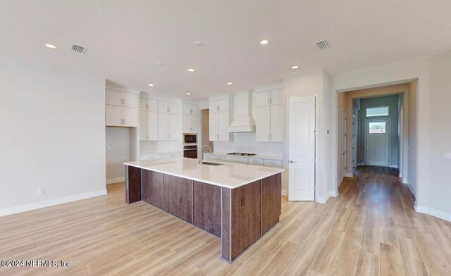 kitchen featuring light wood-style flooring, a sink, visible vents, white cabinetry, and custom exhaust hood