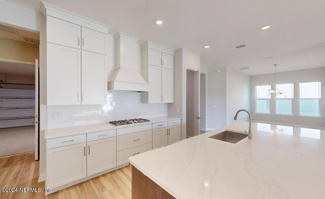 kitchen featuring white cabinets, a sink, custom exhaust hood, stainless steel gas cooktop, and backsplash